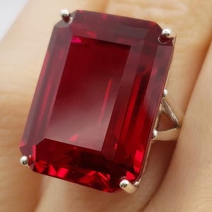 May include: A large, rectangular, deep red gemstone ring with a silver band. The gemstone is set with four small silver prongs. The initials "BB" are in script at the bottom of the image.