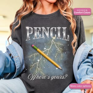 May include: Dark gray sweatshirt with the word "PENCIL" in silver lettering. A yellow pencil with a pink eraser and green stripes is superimposed over a lightning bolt graphic. The text "Where's yours?" is below the pencil.