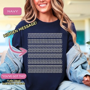May include: Navy blue long-sleeve top with a white geometric design. The top features the text "HIDDEN MESSAGE!" and "YOU'VE GOT THIS". The style is casual.