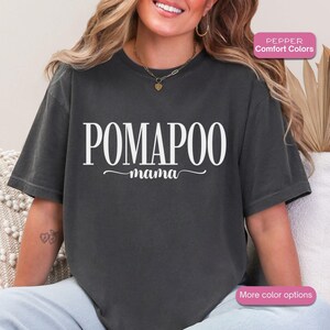 Peut inclure: T-shirt gris foncé avec l'inscription blanche "POMAPOO mama". Le t-shirt a une coupe décontractée et est fait d'une matière douce. Le texte est en gras, avec un "mama" en cursive en dessous.
