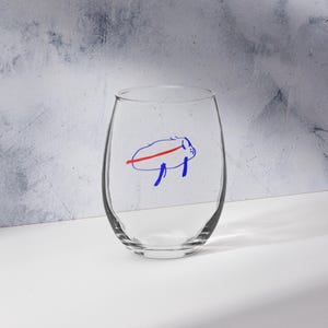Può includere: Un bicchiere da vino senza stelo trasparente con un disegno blu e rosso di un bufalo. Il bicchiere è vuoto e si trova su una superficie bianca. Lo sfondo è grigio chiaro.