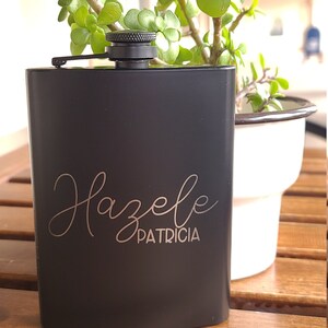 May include: Black metal flask with a silver inscription that reads "Hazelle Patricia".