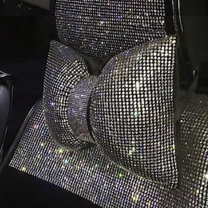 May include: Close-up of car seat covers fully encrusted with sparkling rhinestones. The covers are silver and reflect light, creating a dazzling effect. The seat covers are on a black car seat.