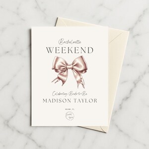 Op de afbeelding: Een witte kaart met de tekst "Bachelorette Weekend" en "Celebrating Bride-to-Be MADISON TAYLOR". Een roze gouden strik illustratie staat in het midden van de kaart. De kaart ligt op een crème-kleurige envelop.