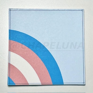 May include: Square sticker with a light blue background and a partial rainbow design in pink, white, and blue. The sticker has a thin black border and the word "HAPELUNA" is faintly visible.