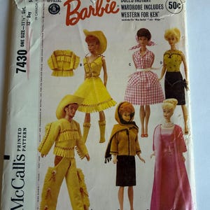 May include: A vintage McCall's 7430 sewing pattern envelope for Barbie and Ken dolls. The front features illustrations of six dolls wearing various outfits, including a yellow western set, a pink gingham dress, and a long pink evening gown.