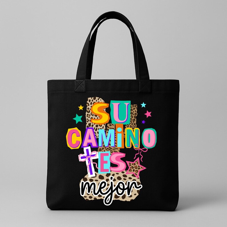Peut inclure: Sac fourre-tout noir avec l'inscription "SU CAMINO ES mejor" en espagnol, aux couleurs vives. Le design comprend un imprim&eacute; l&eacute;opard, des &eacute;toiles et une croix. Le sac a des anses noires et est probablement en toile ou dans un mat&eacute;riau similaire.