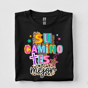 Peut inclure: T-shirt noir avec l'inscription color&eacute;e "SU CAMINO ES MEJOR". Le design comprend une croix, des &eacute;toiles et des motifs l&eacute;opard, cr&eacute;ant un visuel vif et accrocheur.