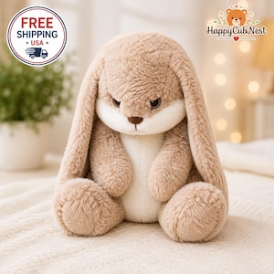 May include: A plush stuffed animal in the shape of a rabbit with long, floppy ears. The rabbit has light brown, textured fur on its head, ears, and limbs, with a smooth, cream-colored patch covering its face, chest, and belly area.