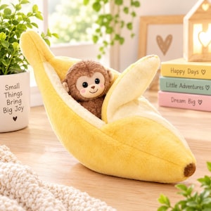 May include: A plush toy featuring a brown monkey nestled inside a soft, yellow banana peel. The monkey has a light brown face, dark eyes, and pink cheeks. The banana peel is textured with a lighter yellow interior and a brown tip at the end.