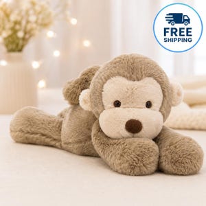 May include: A plush monkey toy with soft, light brown fur and a cream-colored face. The stuffed animal features dark brown eyes, a small dark brown nose, and rounded ears, positioned in a lying-down pose with its front paws tucked forward.