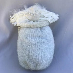 May include: A handmade white angel doll with a knitted body and a feathered halo. The doll has a soft, textured appearance, with a light blue knitted body and a white feathered halo. The doll is a decorative item.