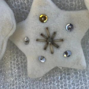 May include: Close-up of a white felt star decoration. The star is adorned with gold and silver sequins, and a central beaded design. Likely for festive or seasonal use.