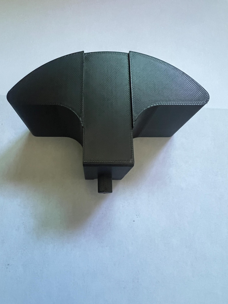 May include: A black, 3D-printed object with a unique shape. It features a curved, fan-like top section and a rectangular base with a cylindrical projection. The object appears to be made of a textured material.