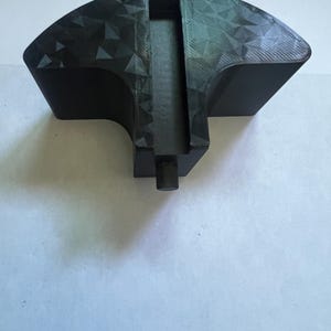 May include: A black, geometric-patterned object with a fan-like shape. It features a central rectangular channel and a cylindrical projection at the base. The surface has a textured, triangular design.