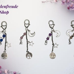 May include: Four silver-toned keychains with heart-shaped clasps. Each keychain features a chain with beads, stars, and a tree of life charm. The keychains have different colored beads: blue, pink, and purple. The text "Schadenfreude Shop" is at the top.