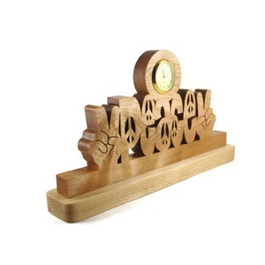May include: Wooden clock with the word "Peace" spelled out in peace signs. The clock is on a wooden base.