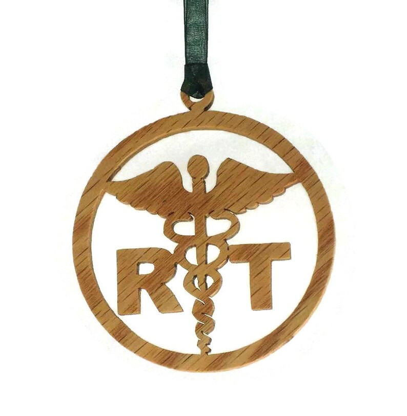 May include: A wooden ornament with a round shape and a brown color. The ornament features a medical symbol with a snake and wings, and the letters "RT" are cut out below the symbol.