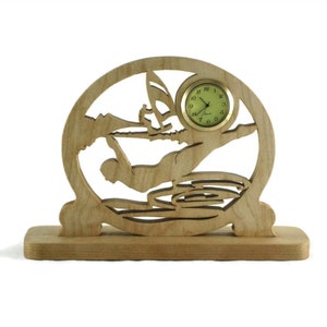 May include: A wooden clock with a silhouette of a person diving into water. The clock face is round and has a gold rim. The clock is on a wooden base.