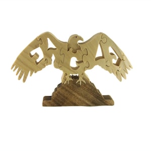May include: Wooden puzzle of an eagle with its wings spread, the eagle's body is made up of the word "eagle" in puzzle pieces. The eagle is standing on a wooden base.