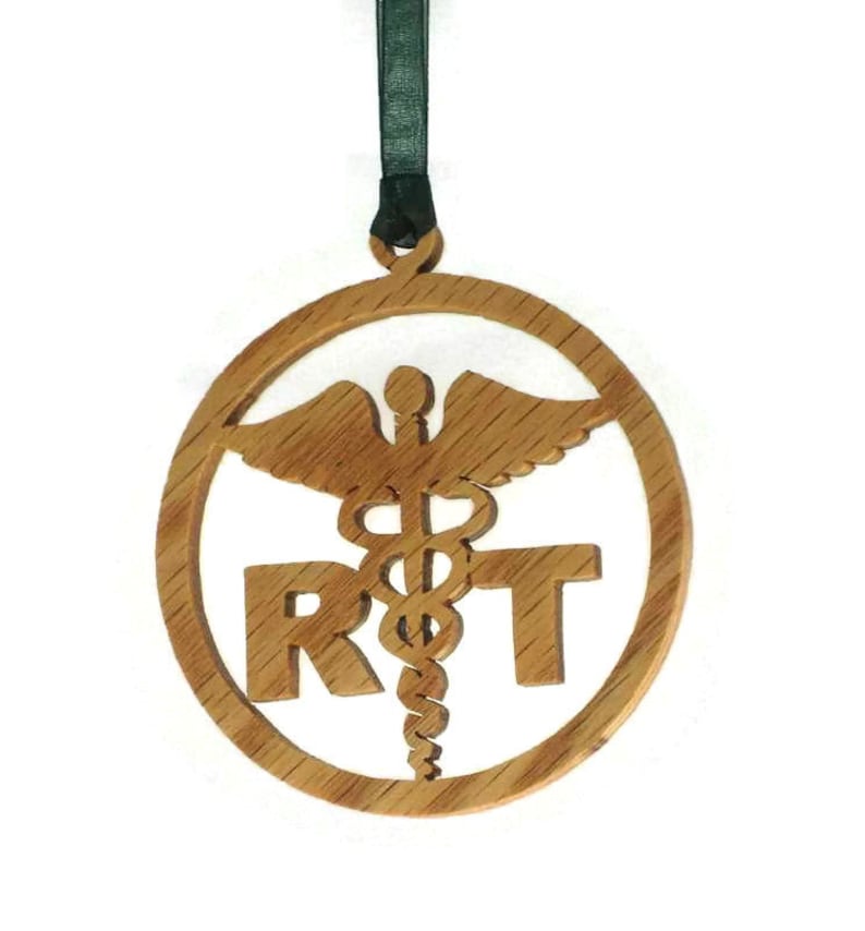 May include: A wooden ornament with a green ribbon. The ornament is round and features a cutout of the medical symbol, a snake wrapped around a staff with wings, and the letters "RT".