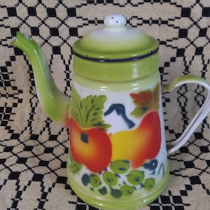 May include: A green enamel teapot with a white lid and a painted design of apples, grapes, and leaves. The teapot has a handle and a spout.