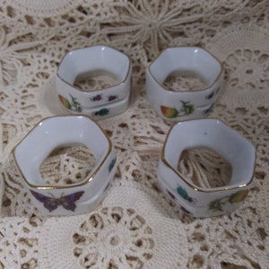 May include: Set of four white porcelain napkin rings with gold trim. Each ring features a different floral and insect design.
