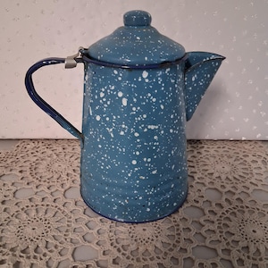 May include: A blue enamelware coffee pot with white speckles. The pot has a lid, a spout, and a handle. The rim and handle are dark blue. This vintage-style pot is suitable for camping or kitchen use.