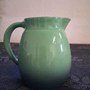 May include: A white ceramic mug with a black handle and the text "But First, Coffee" in a black, bold font. The mug is sitting on a white surface. The mug is approximately 4 inches tall.