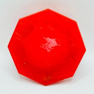K&ouml;nnte beinhalten: Ein leuchtend rotes achteckiges Tablett mit glatter, gl&auml;nzender Oberfl&auml;che. Die Fl&auml;che zeigt ein dezentes, wirbelndes wei&szlig;es Marmormuster, das sich in der Mitte konzentriert und einen Kontrast zum kr&auml;ftigen, einfarbigen roten Hintergrund bildet.