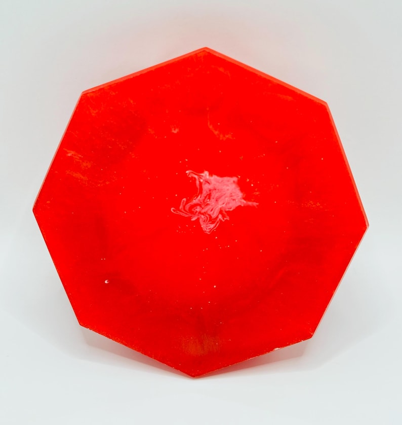 K&ouml;nnte beinhalten: Ein leuchtend rotes achteckiges Tablett mit glatter, gl&auml;nzender Oberfl&auml;che. Die Fl&auml;che zeigt ein dezentes, wirbelndes wei&szlig;es Marmormuster, das sich in der Mitte konzentriert und einen Kontrast zum kr&auml;ftigen, einfarbigen roten Hintergrund bildet.