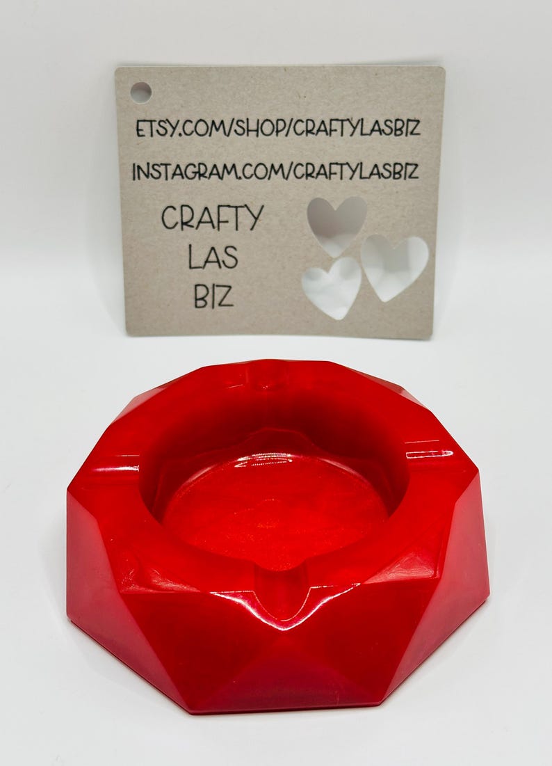 K&ouml;nnte beinhalten: Ein leuchtend roter, facettierter, geometrisch geformter Aschenbecher mit glatter, gl&auml;nzender Oberfl&auml;che. Dahinter befindet sich eine rechteckige, hellbraune Karte mit dem Text "ETSY.COM/SHOP/CRAFTYLASBIZ", "INSTAGRAM.COM/CRAFTYLASBIZ", "CRAFTY LAS BIZ" und drei herzf&ouml;rmigen Ausstanzungen.