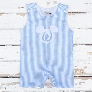 May include: Light blue and white striped seersucker romper with a white Mickey Mouse-shaped applique featuring a blue letter "W". The romper has button closures on the shoulders and a tag that reads "Dressy Jessy Smocking".