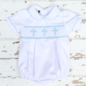 May include: White baby romper with short sleeves and a Peter Pan collar. The romper features light blue trim and three embroidered crosses across the chest. The fabric is gathered at the waist, creating a bubble shape.