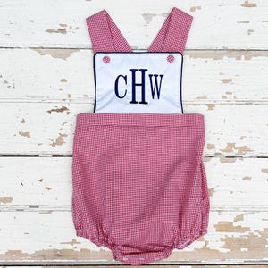 May include: Red and white gingham baby bubble romper with a white bib. The bib features navy blue embroidered initials "CHW" and is trimmed with navy blue piping. The romper has adjustable straps and button details.