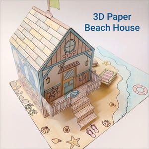 Op de afbeelding: Een 3D papieren strandhuismodel in lichtblauw en bruin. Het model heeft een veranda, trappen en een kleine vlag. De tekst "3D Paper Beach House" is zichtbaar. Het model staat op een strandscène met een getekende oceaan, strandstoel en schelpen.