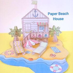 Op de afbeelding: Een papieren strandhuis-diorama met een blauwe oceaan, zandstrand en palmbomen. Het huis heeft een ankersymbool en een vlag. De scène bevat ligstoelen, een parasol en een reddingsboei. Tekst op de afbeelding luidt "Paper Beach House."