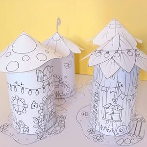 Puede incluir: Cuatro casas de hadas de papel blanco con detalles en negro. Las casas tienen diferentes diseños de techo, incluyendo formas de hongo y hoja. Cada casa presenta una puerta, ventanas y elementos decorativos como luces de cadena y patrones florales. Las casas están sobre bases de papel.