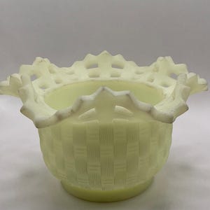 Puede incluir: Un cuenco de vidrio custard de color amarillo pálido con un patrón de tejido de cesta en el cuerpo exterior. El cuenco tiene un borde ancho y acampanado con un diseño decorativo de celosía calada y un borde festoneado muy característico.
