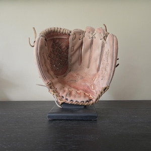 Peut inclure: Un gant de baseball en cuir beige avec un design de toile tissée, des lacets beiges et une signature sur la paume. Le gant est monté sur un support rectangulaire noir, affichant clairement la signature George Brett et le texte du modèle.
