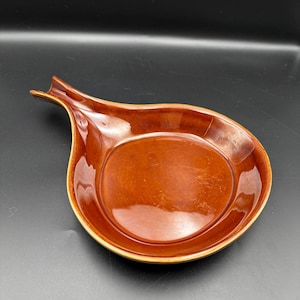 May include: A brown ceramic onion-shaped serving dish with a handle. The dish has a glossy finish and a light brown rim. The interior is a darker shade of brown.