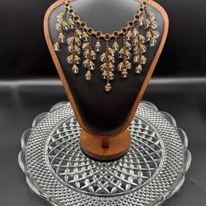 May include: A multi-strand necklace featuring a brass chain base with numerous dangling clear faceted crystal beads. The beads are attached to the chain with small brass caps, creating a layered, cascading effect across the neckline.