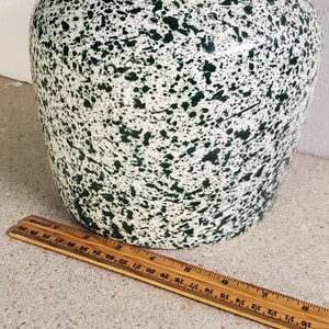 May include: A ceramic jar with a lid, featuring a white base and a speckled pattern of dark green. The jar is approximately 10 inches tall and 8 inches wide. A wooden ruler is placed next to the jar.