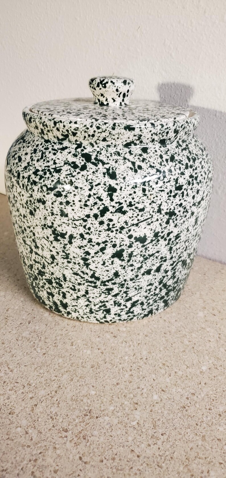 May include: A ceramic jar with a lid, featuring a white base and a speckled green pattern. The jar has a rounded body and a small knob on the lid. The design gives a rustic, handcrafted feel. Ideal for kitchen storage.