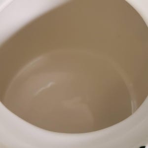 May include: A white ceramic mug with a black handle and the text "But First, Coffee" in a bold, black font. The mug is set against a blurred background, suggesting a cozy setting.