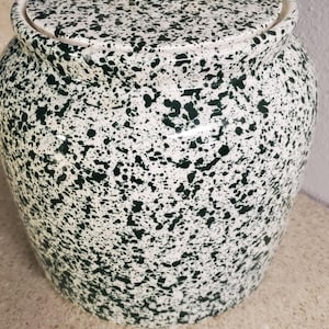 May include: A ceramic jar with a lid, featuring a speckled pattern of dark green spots on a white background. The jar has a rounded shape and a small knob on the lid. The jar is likely used for storage.