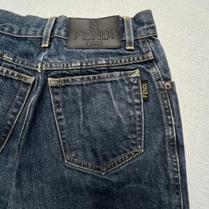 May include: Dark wash denim jeans with a leather Fendi Jeans label on the back waistband. The jeans have a classic five-pocket design with a small Fendi label on the back pocket.