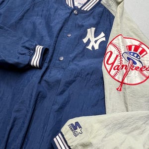 May include: A navy blue and gray vintage Starter jacket featuring the New York Yankees logo. The jacket has a snap-front closure, white accents, and a large Yankees logo patch on the sleeve. The Starter logo is visible on the cuff.