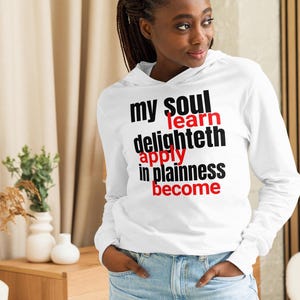 Könnte beinhalten: Weißer Langarm-Hoodie mit dem Text "my soul learn delighteth apply in plainness become" in Schwarz und Rot. Der Hoodie hat eine Kapuze und lange Ärmel.