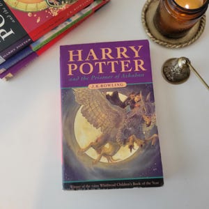 May include: A copy of "Harry Potter and the Prisoner of Azkaban" by J.K. Rowling. The book has a purple cover with the title in yellow. The cover art depicts a winged creature in front of a full moon. The book is a winner of the Whitbread Children's Book of the Year.